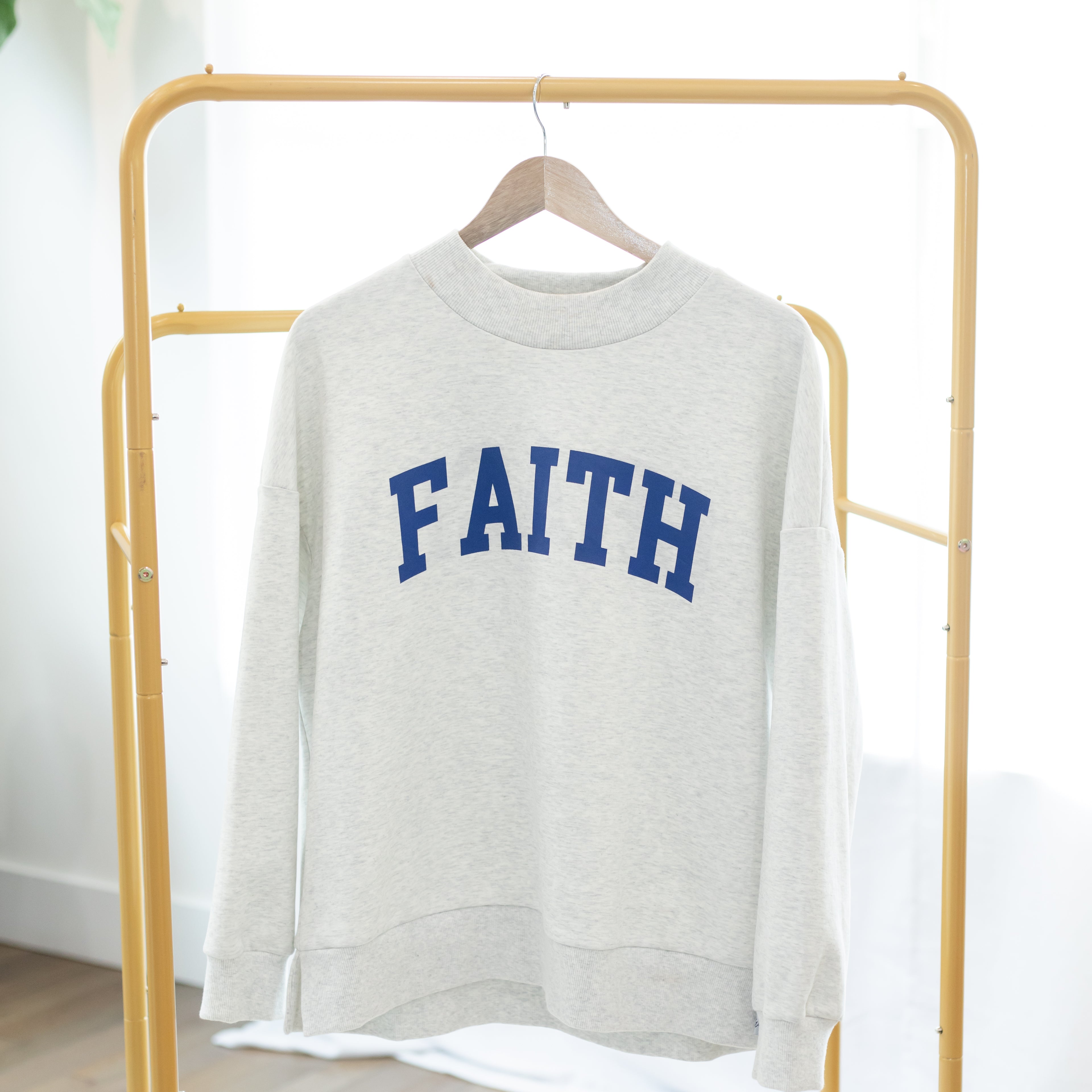 Gray sweatshirt with 'FAITH' printed in blue on a gold rack.