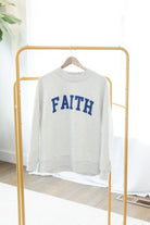 Gray sweatshirt with 'FAITH' printed in blue on a gold rack.