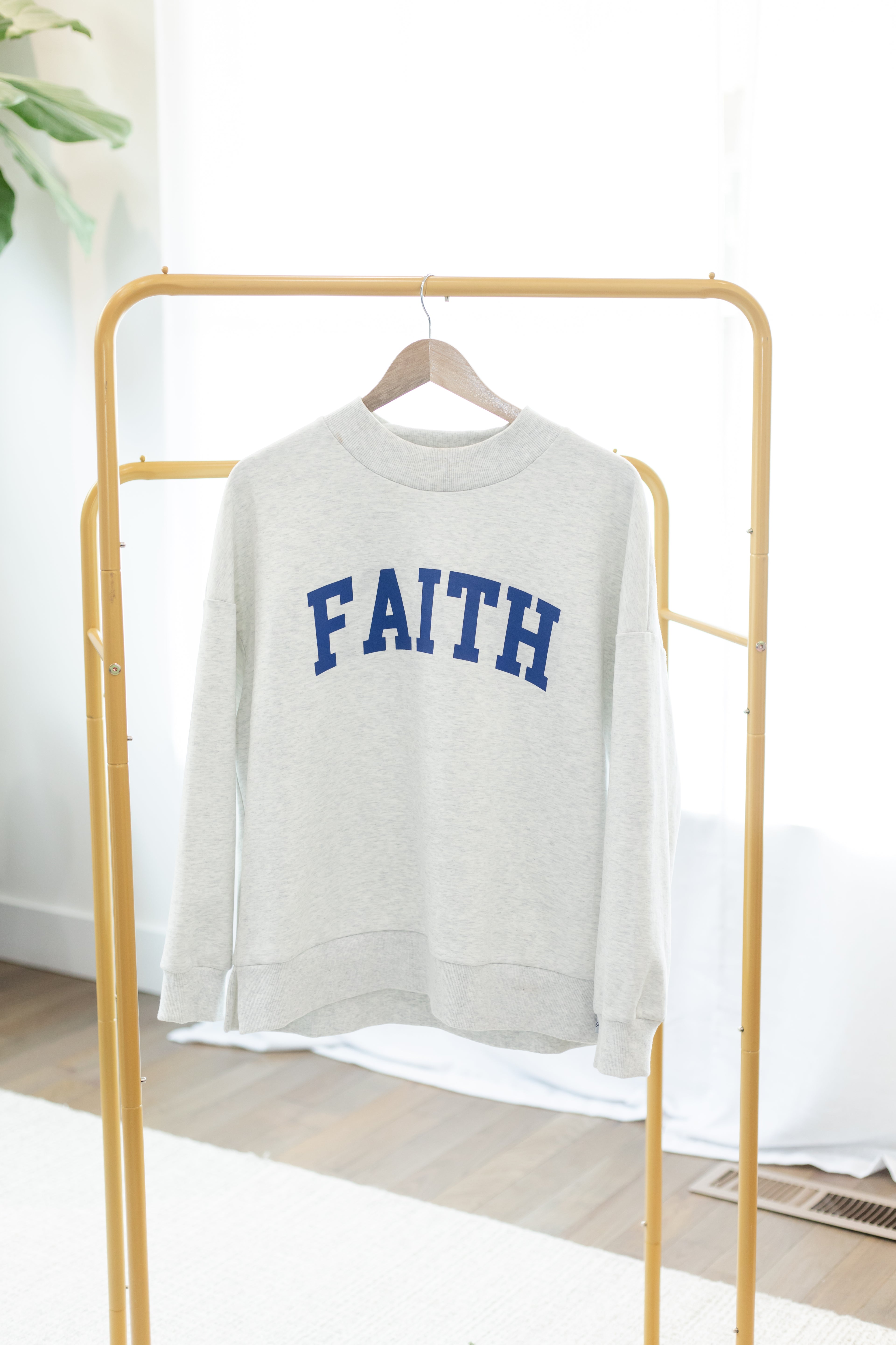 Gray sweatshirt with 'FAITH' printed in blue on a gold rack.