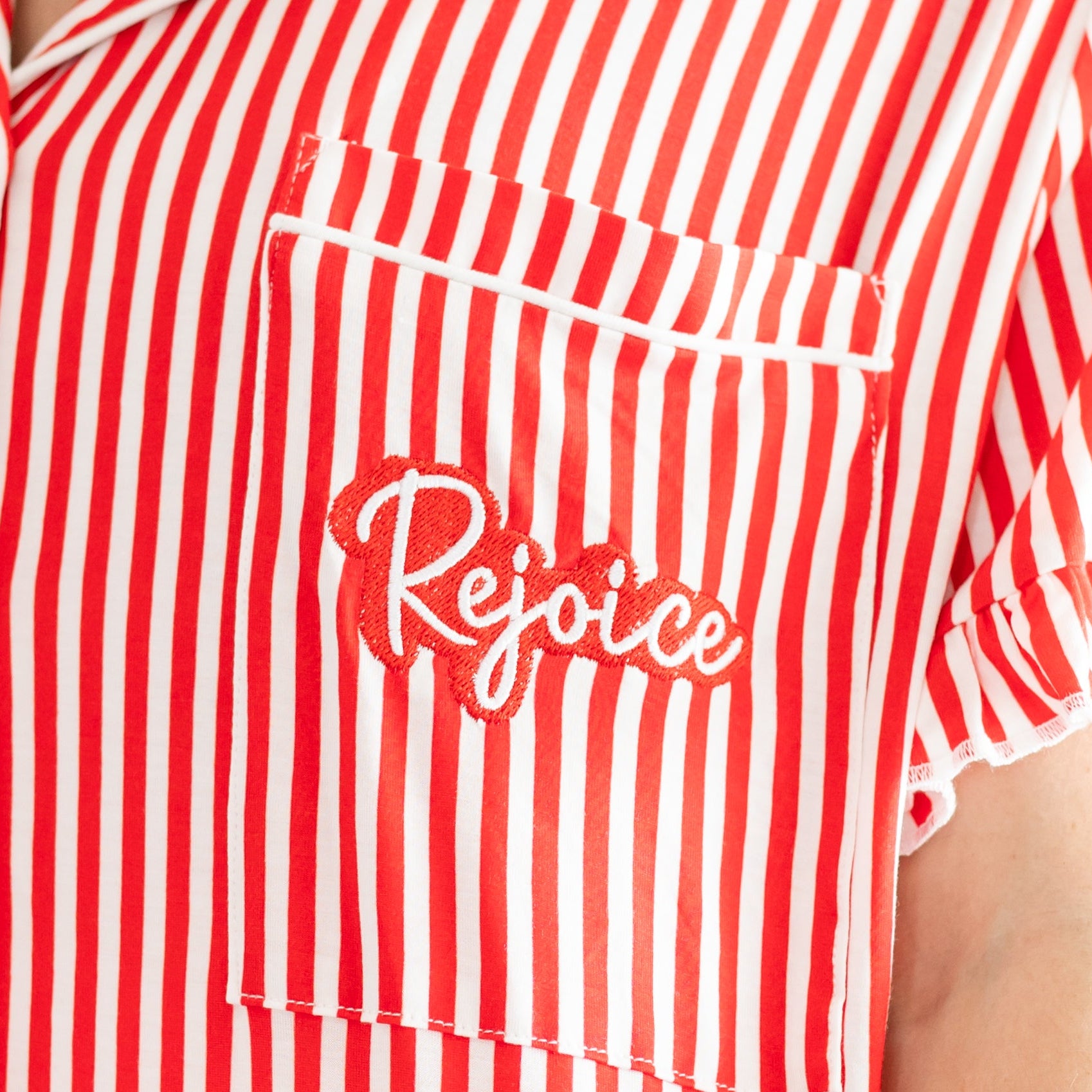 Woman wearing a red and white striped shirt with 'Rejoice' logo.