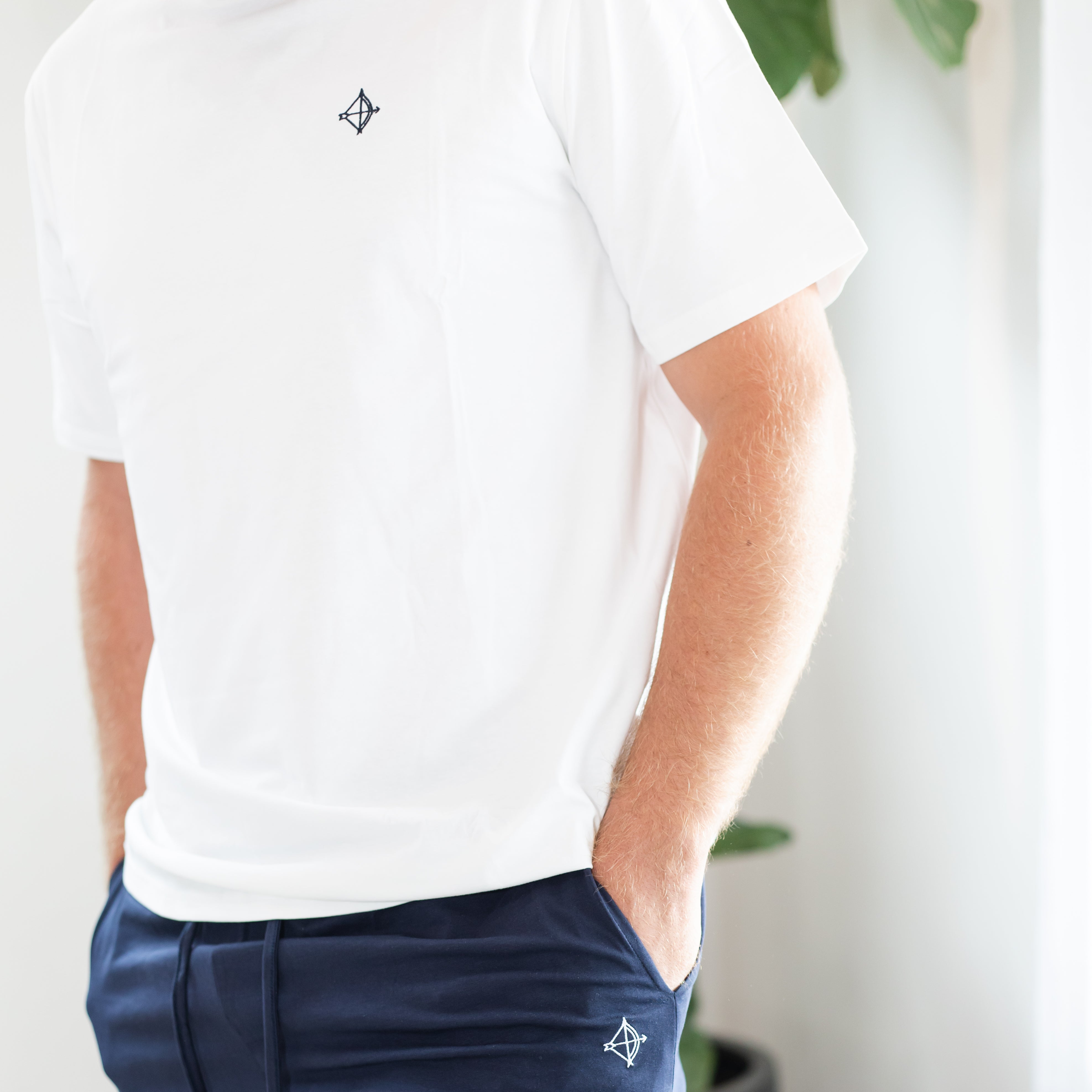 Person wearing a white polo shirt and navy pants with a logo, standing indoors.